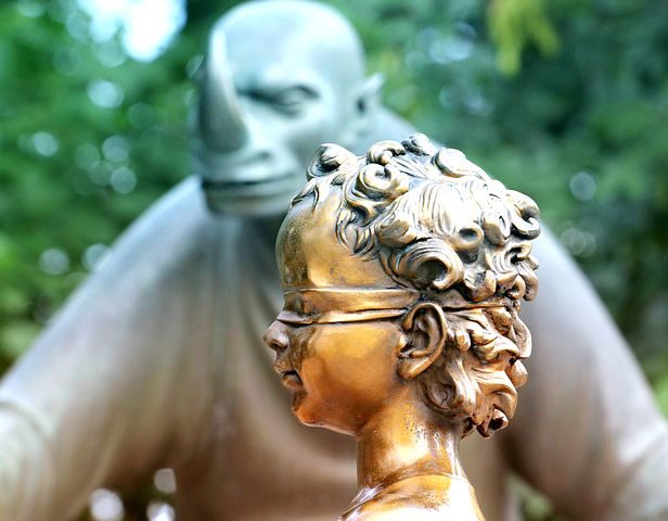 Beitragsbild: Das Bild zeigt den Kopf mit verbundenen Augen vor einer goldenen Figur vor einer Figur mit Horn auf der Nase